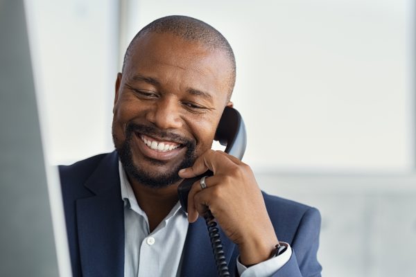 Close up face of mature businessman working on computer and talk Close up face of mature businessman working on computer and talking on phone. Mature african man talking on mobile phone at desk in office. Smiling manager working at desk with copy space.